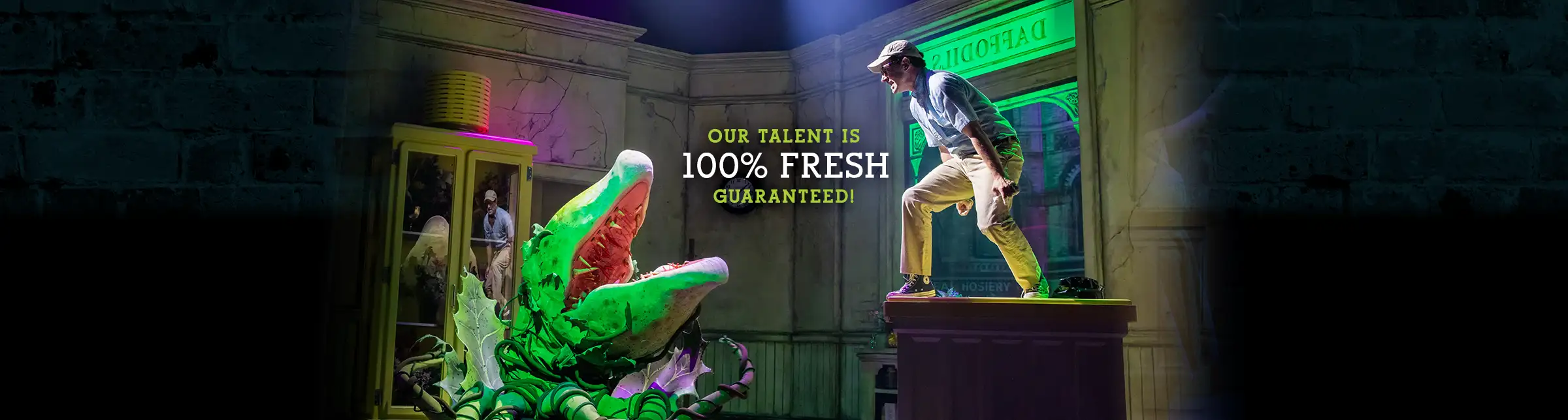 Scene from Little Shop of Horrors featuring Seymour confronting the giant Audrey II plant on stage at the Westside Theatre, with the tagline ‘Our talent is 100% fresh guaranteed.